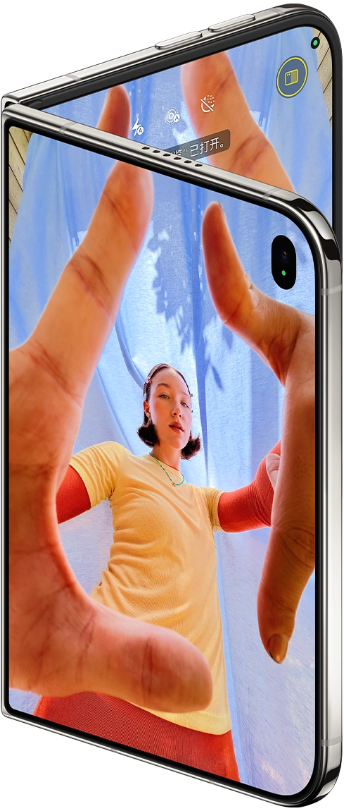 星光白色 iPhone Duo 呈微微展开状态，外屏展示相机 app，以及 Center Stage 前置摄像头，内屏展示照片 app 图库。