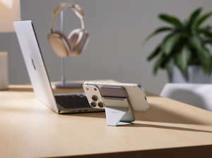 Moft MagSafe Wallet Stand, back exterior, iPhone in landscape orientation, attached to wallet stand in portrait orientation, placed on a desk next to a MacBook