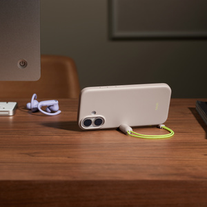 Beats Kickstand Case, lime stone color attached to iPhone 17, side view, lying on a wooden desk in landscape orientation with lanyard magnetic connector attached to side holding iPhone upright