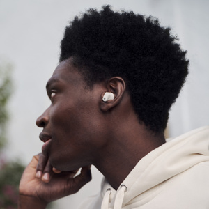 Person wearing Beats Studio Buds + earbuds in Ivory, toggling the on-device controls in outdoor environment. 