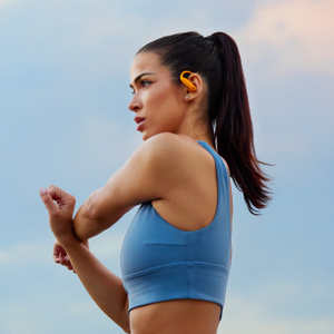 Angled view of Powerbeats Pro 2 wireless earbuds in Electric Orange, showing flexible secure-fit earhooks, on-ear buttons and tactile volume rockers.