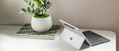 A white pot with green leaves next to a tablet on a desk.