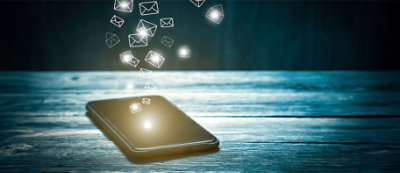 A smartphone rests on a table with glowing icons resembling messages floating above it