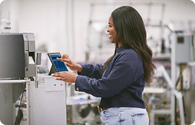 A woman using a tablet to control a machine in a manufacturing setting.