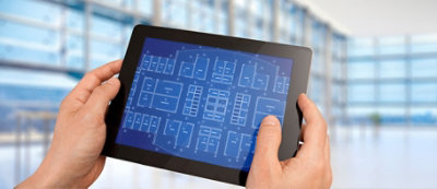 A person holds a tablet displaying digital architectural blueprints