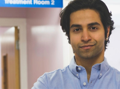 A man in a blue shirt stands confidently in front of a sign.