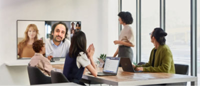A group of people in a conference room watching a video conference on a large screen.