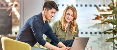 Two person sit together in an office working on a laptop